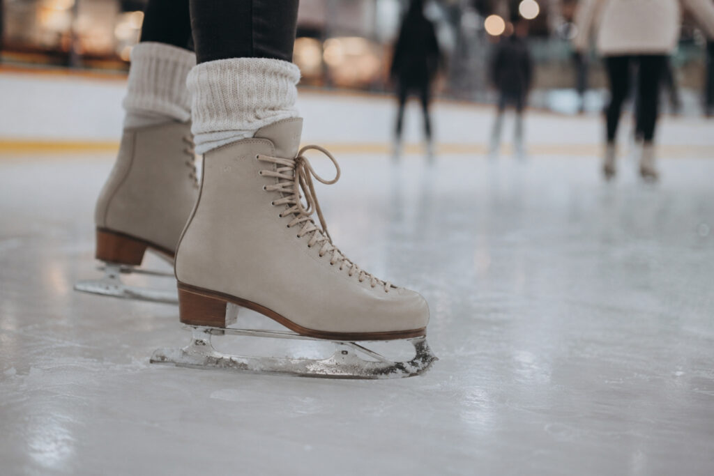 Eiskunstlauf-Schlittschuhe stehen auf einer glatten Eisbahn, im Hintergrund sind verschwommene Passanten zu sehen.